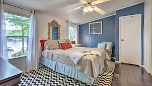 A bedroom with a bed, a ceiling fan, a window with curtains, a mirror, and a door.