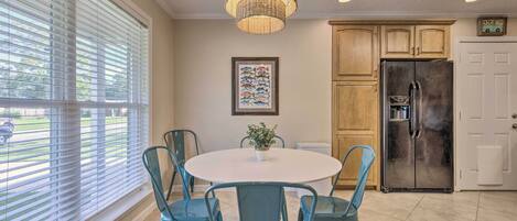 A kitchen with a round table, teal chairs, a hanging light fixture, and wooden cabinets.