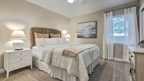 A bedroom with a bed, nightstands, a ceiling fan, a window with curtains, and a painting on the wall. - Ocean Springs Home w/ Bikes < 1 Mile to Beach! (Ocean Springs)