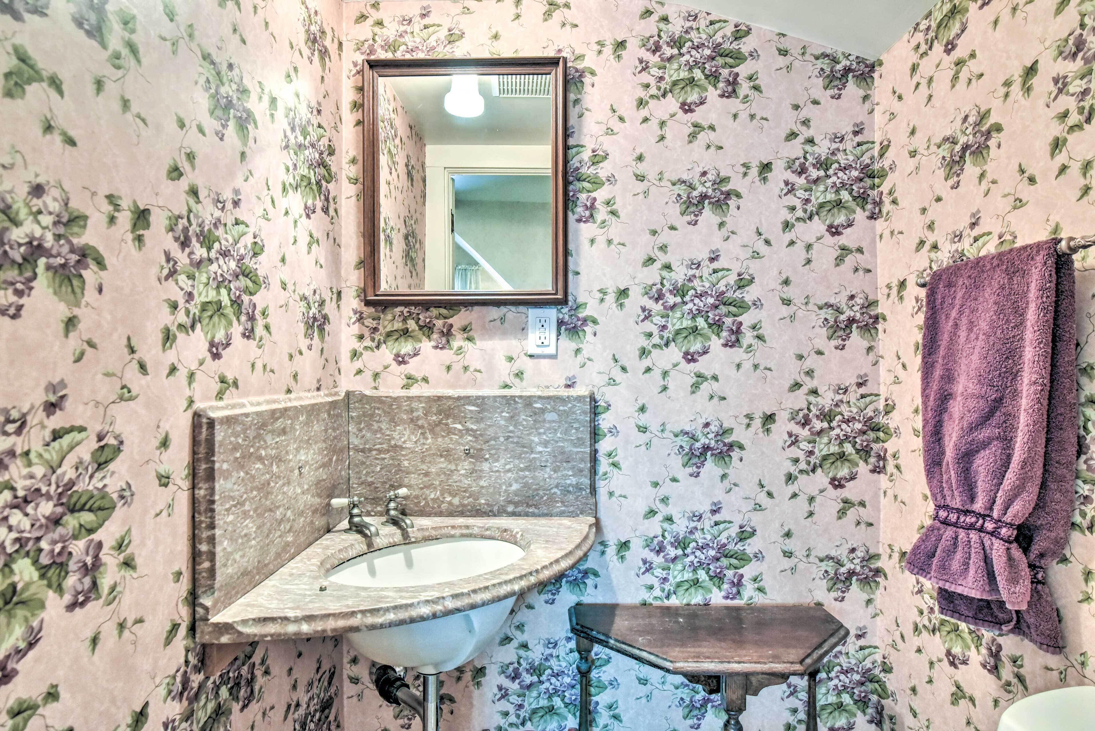 Ein Badezimmer mit blumigem Wandpapier, einem Waschbecken inklusive Spiegel und einem Handtuchhalter.