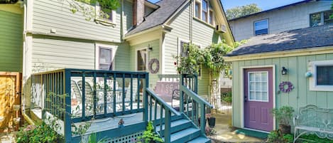 A two-story house with a front porch, a staircase, and a small garden area with potted plants.