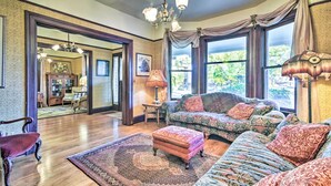 A spacious living room with a large window, a chandelier, and a patterned rug. - Historical Portland Home < 2 Mi to Downtown! (Portland)