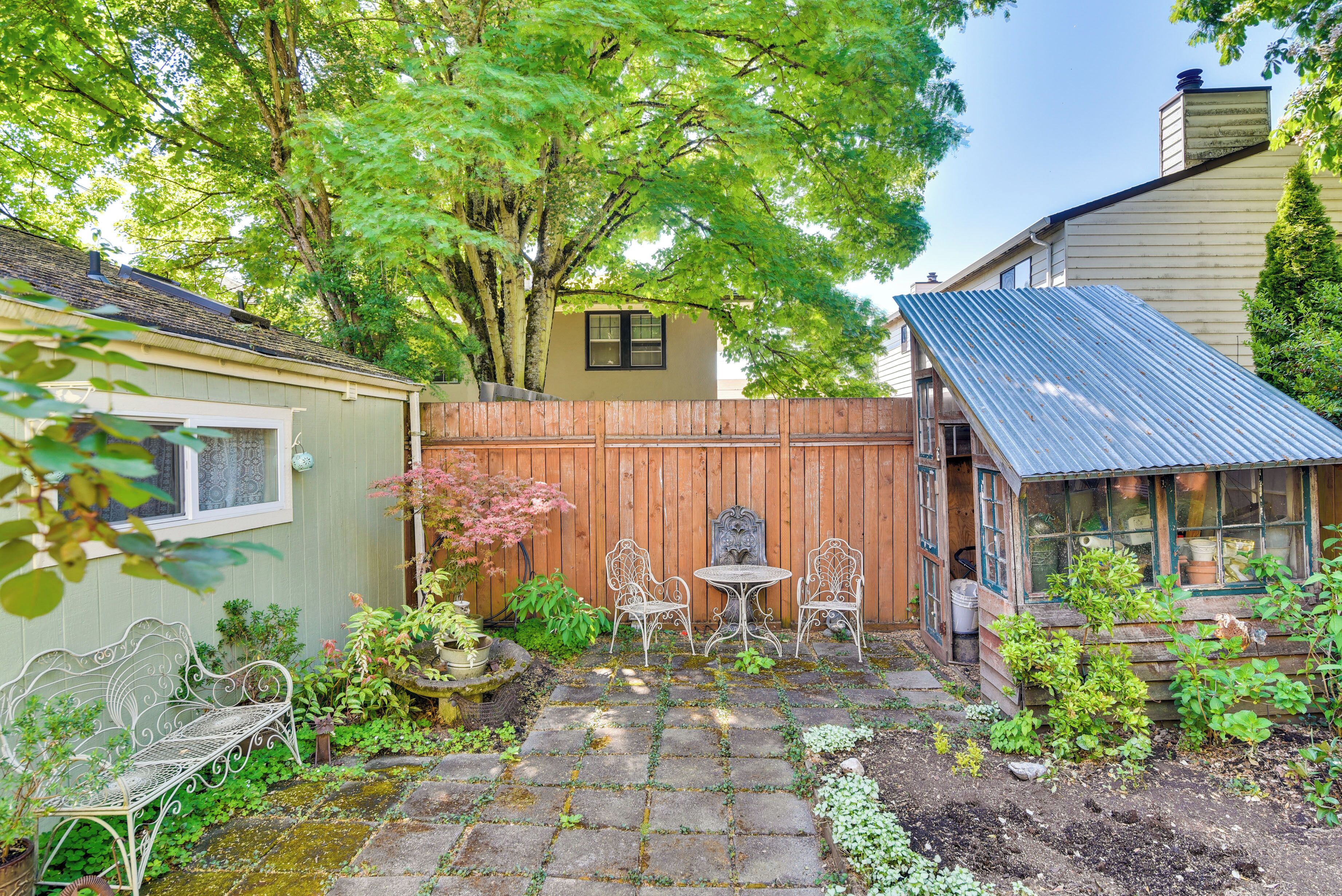 A garden with a wooden fence, a metal bench, and a table with chairs.