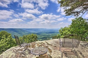 A metal chair and table on a rocky outcrop overlooking a valley.