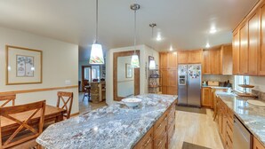 A kitchen with wooden cabinets, granite countertops, a stainless steel refrigerator, and pendant lighting. - Deck & Beach Access: Lake Tahoe Shoreside Retreat! (Zephyr Cove)