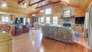 A spacious living area with a large sofa, wooden flooring, a stone fireplace, and a television. - Riffle Run Cabin: River Access, Hot Tub, Game Room (Ellijay)