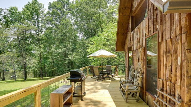 A wooden deck with outdoor furniture, a grill, and a view of the surrounding forest. - Cozy Georgia Abode w/ Deck, Fire Pit & Lake Access (Menlo)