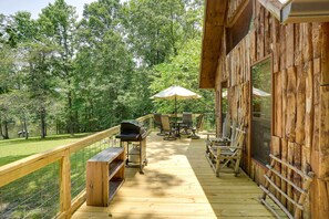 Un patio in legno con mobili da esterno, un barbecue e vista sulla foresta circostante.