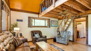 A cozy living room with a brown leather sofa, a patterned armchair, a wooden coffee table, and a staircase leading to an upper level. - Cozy Georgia Abode w/ Deck, Fire Pit & Lake Access (Menlo)