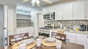 Una cocina moderna con gabinetes blancos, microondas, estufa y una mesa de comedor con platos y tazas.