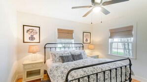 Une chambre à coucher comprenant un lit, des tables de chevet, un ventilateur de plafond et des œuvres d’art encadrées accrochées aux murs.