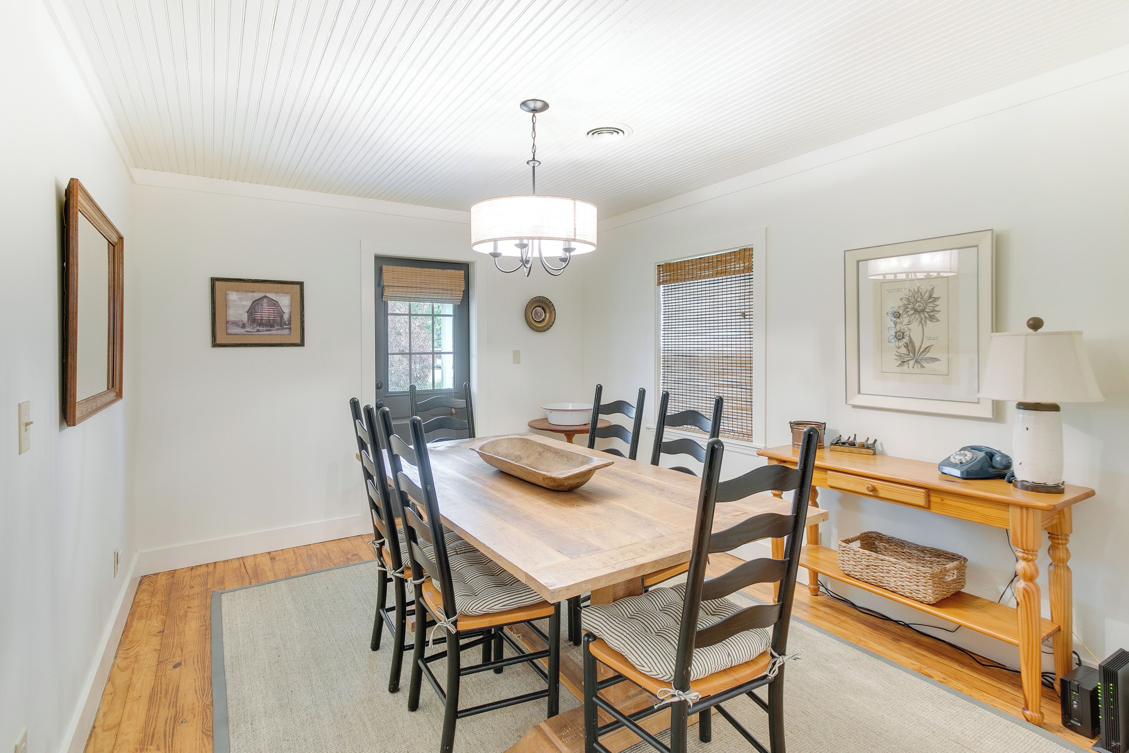 A dining area with a wooden table, chairs, a chandelier, and a window with blinds.