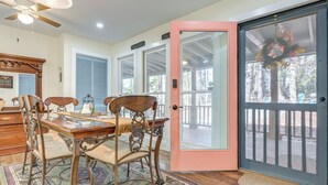 Uma área de refeições com mesa e cadeiras de madeira, tapete estampado e porta de vidro que dá para um deck externo.