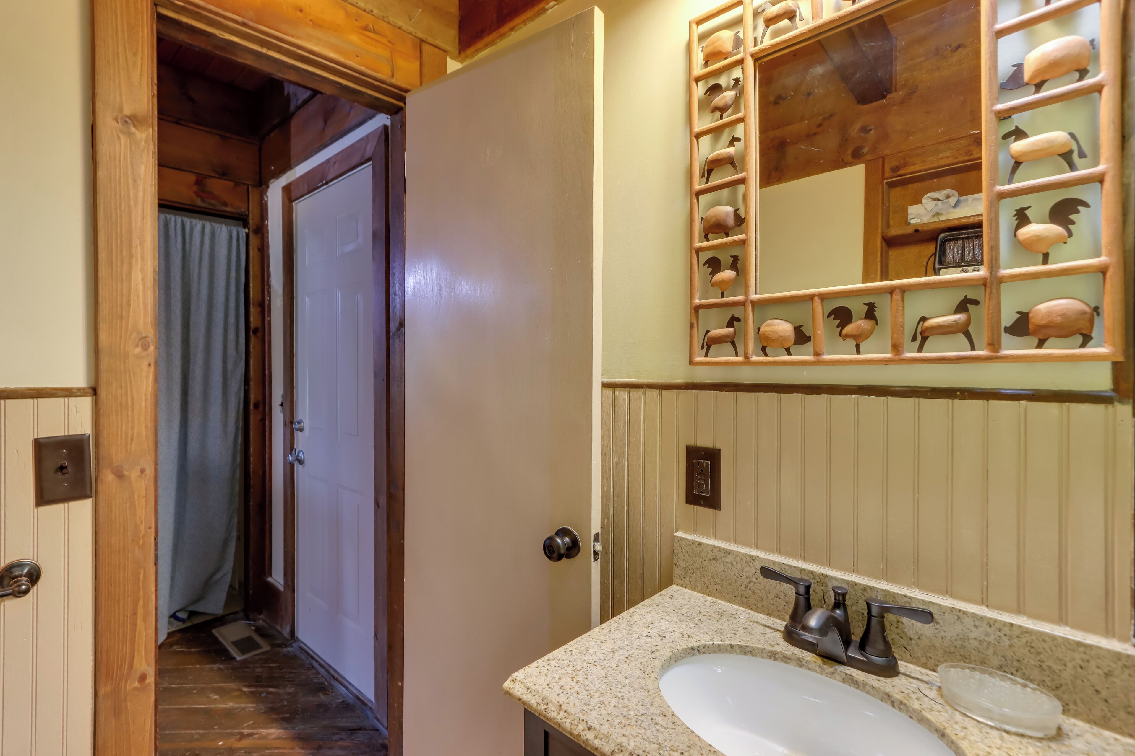 A bathroom with a wooden door, a sink with a mirror, and a decorative sheep mirror above the sink.