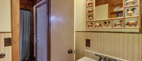 A bathroom with a wooden door, a sink with a mirror, and a decorative sheep mirror above the sink.