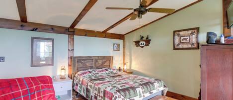 A cozy bedroom with a bed, a wooden bench, a red chair, a ceiling fan, and a dresser.