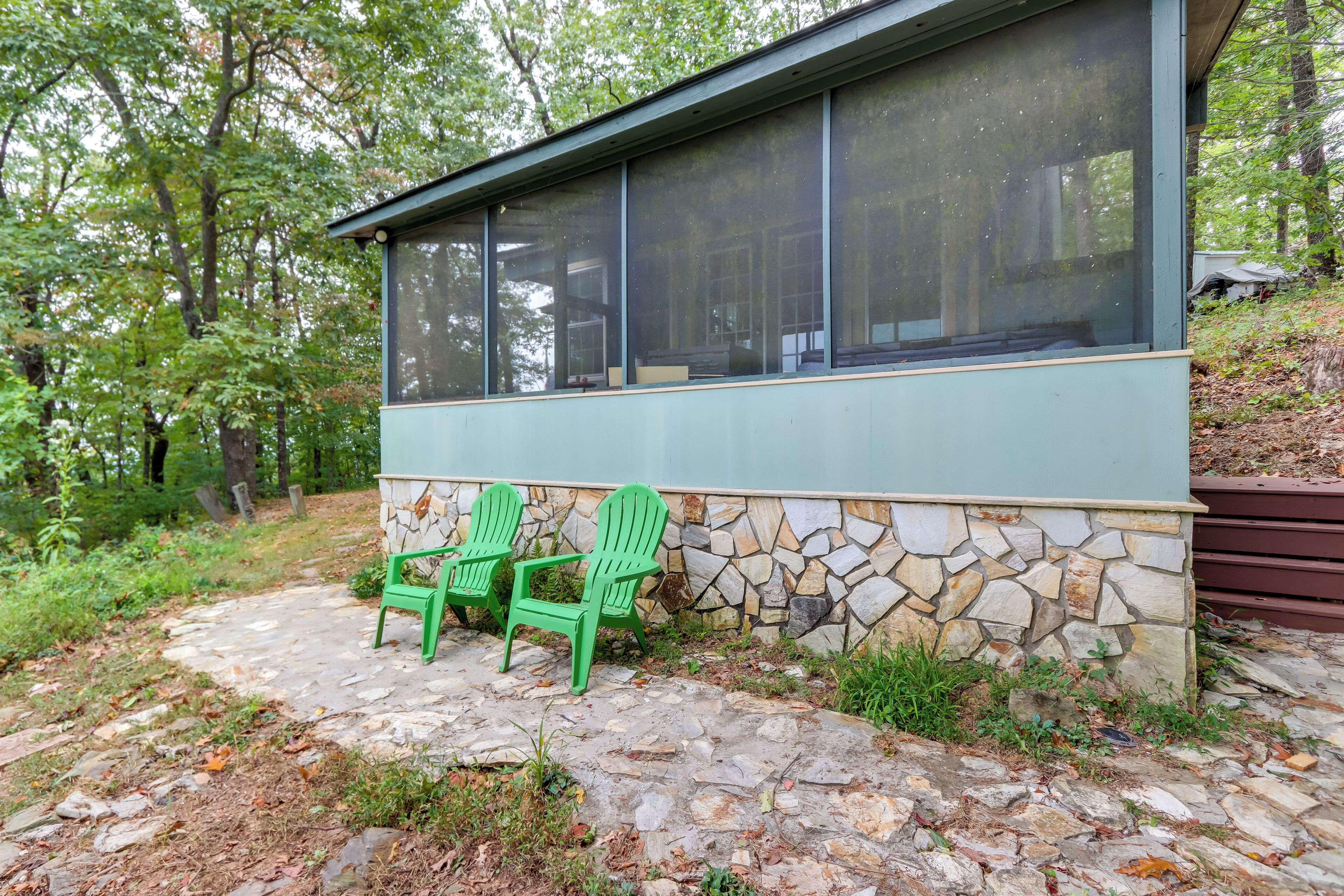 Ein modernes Gebäude mit Natursteinfassade und großen Fenstern. Vor der Fassade stehen zwei grüne Adirondack-Stühle.
