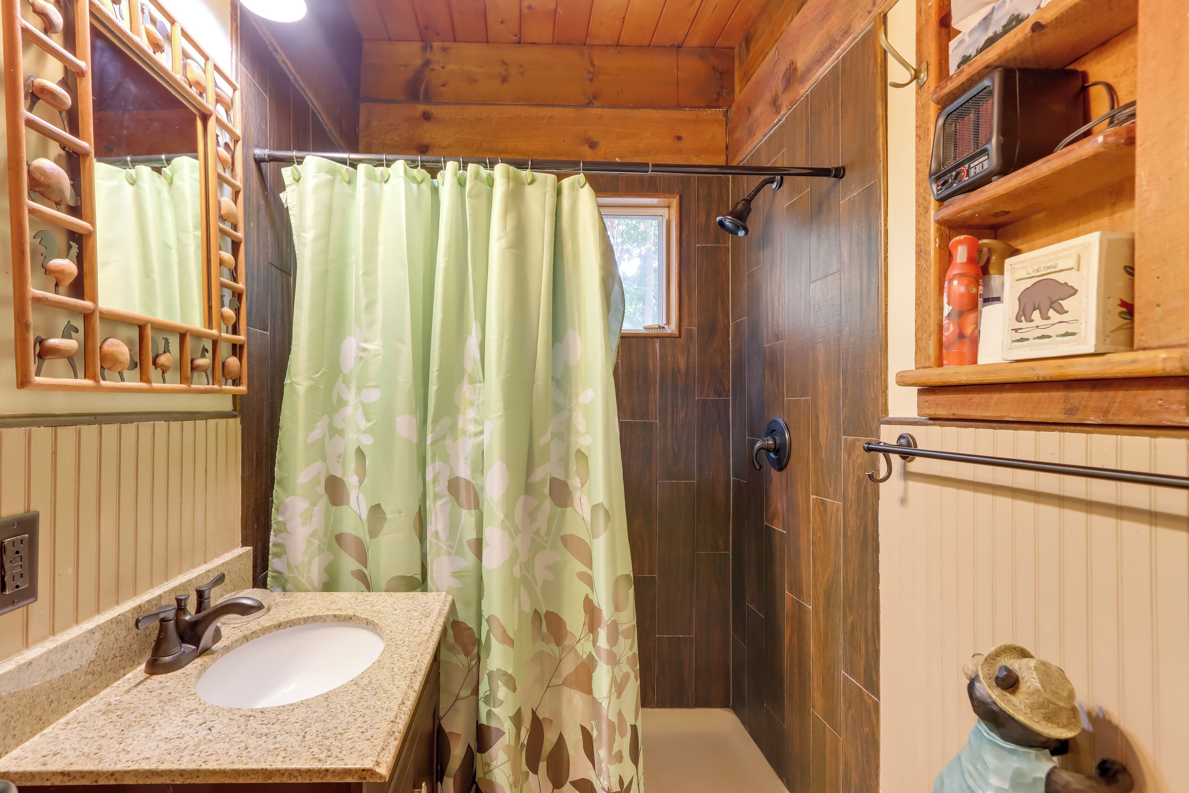 Un baño con tocador de madera, lavamanos, cortina de ducha y estante con artículos de aseo.