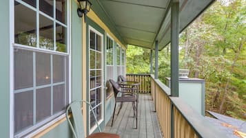 A covered porch with a view of a forest, featuring a table and chairs.