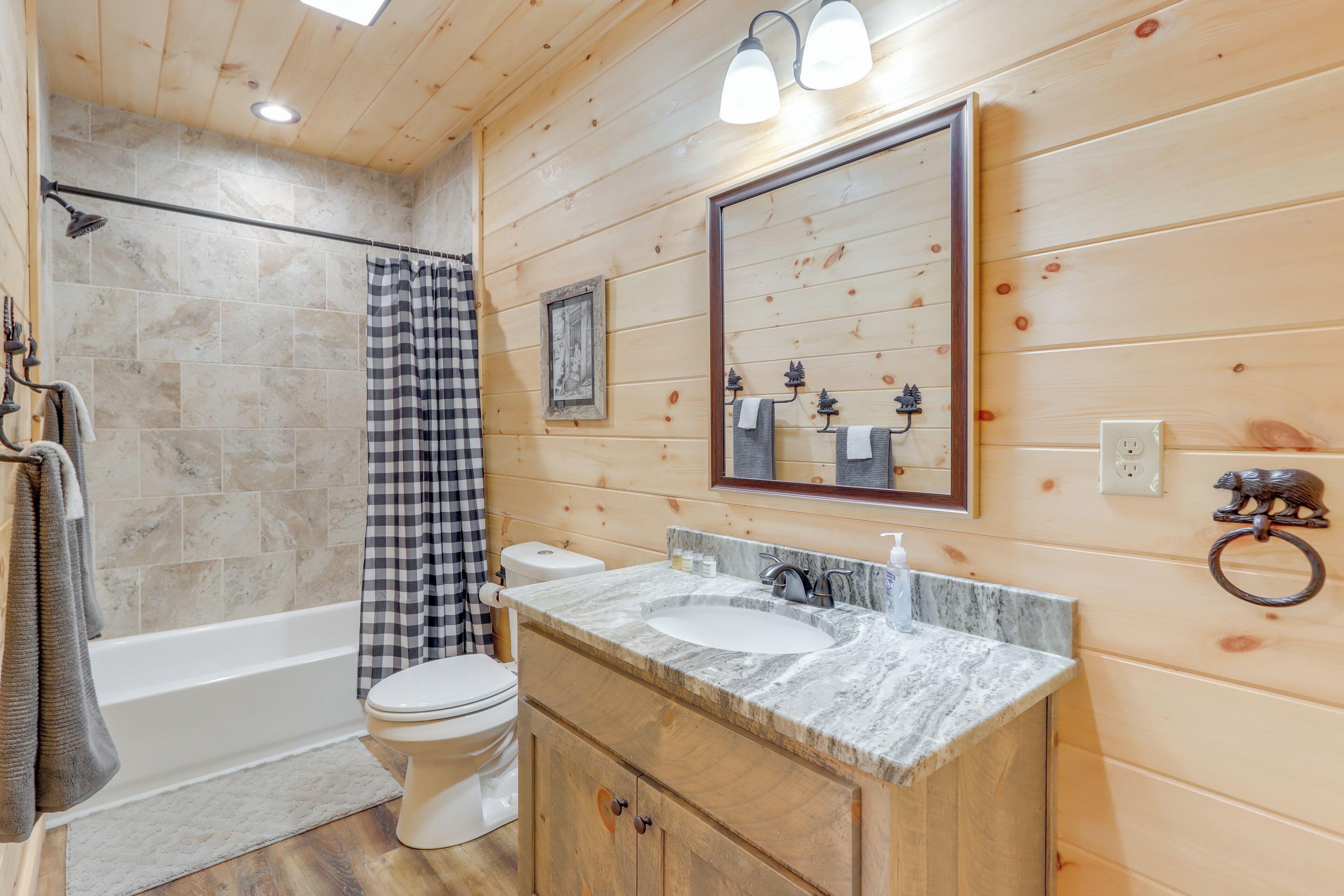 A bathroom with a wooden interior, a bathtub, a toilet, and a vanity with a sink and mirror.