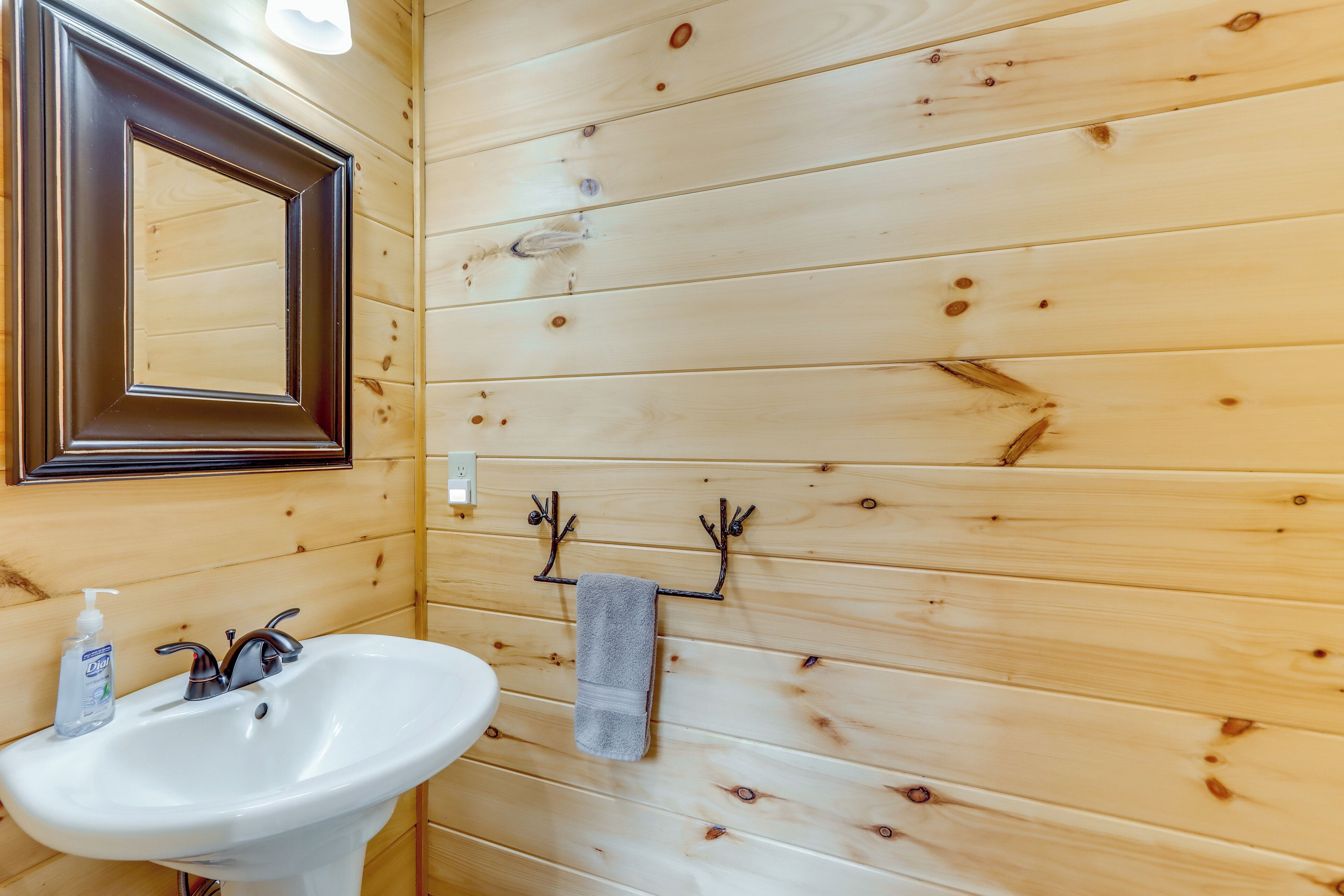 Un baño con paneles de madera, un lavamanos blanco, un espejo y un perchero para toallas.
