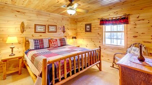 A wooden cabin bedroom with a bed, a nightstand, a table, a chair, a window, and a ceiling fan. - Lakefront Blue Ridge Cabin w/ Hot Tub! (Blue Ridge)