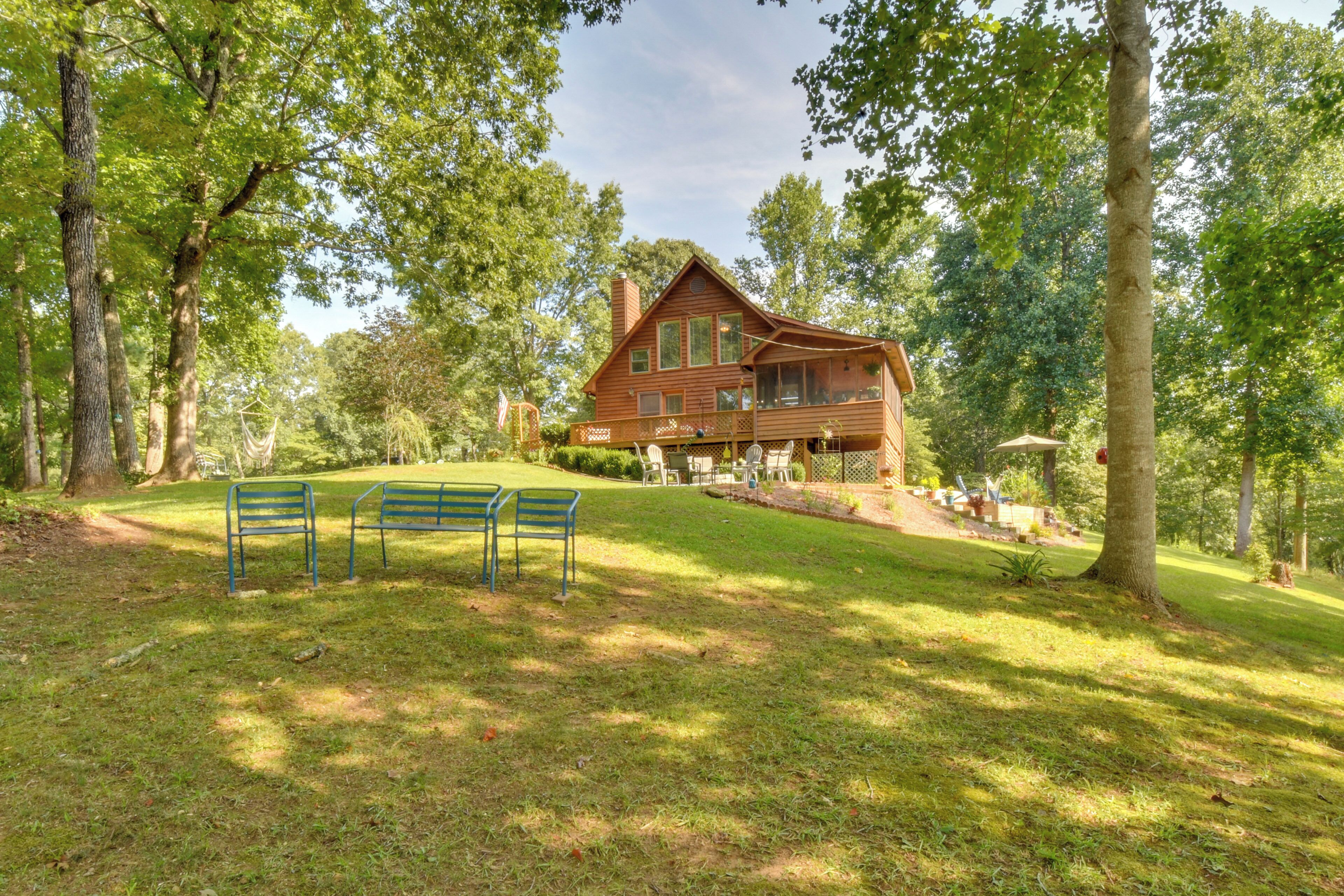 Une cabane en bois dotée d’une terrasse, entourée d’arbres et bordée d’une pelouse avec des bancs.