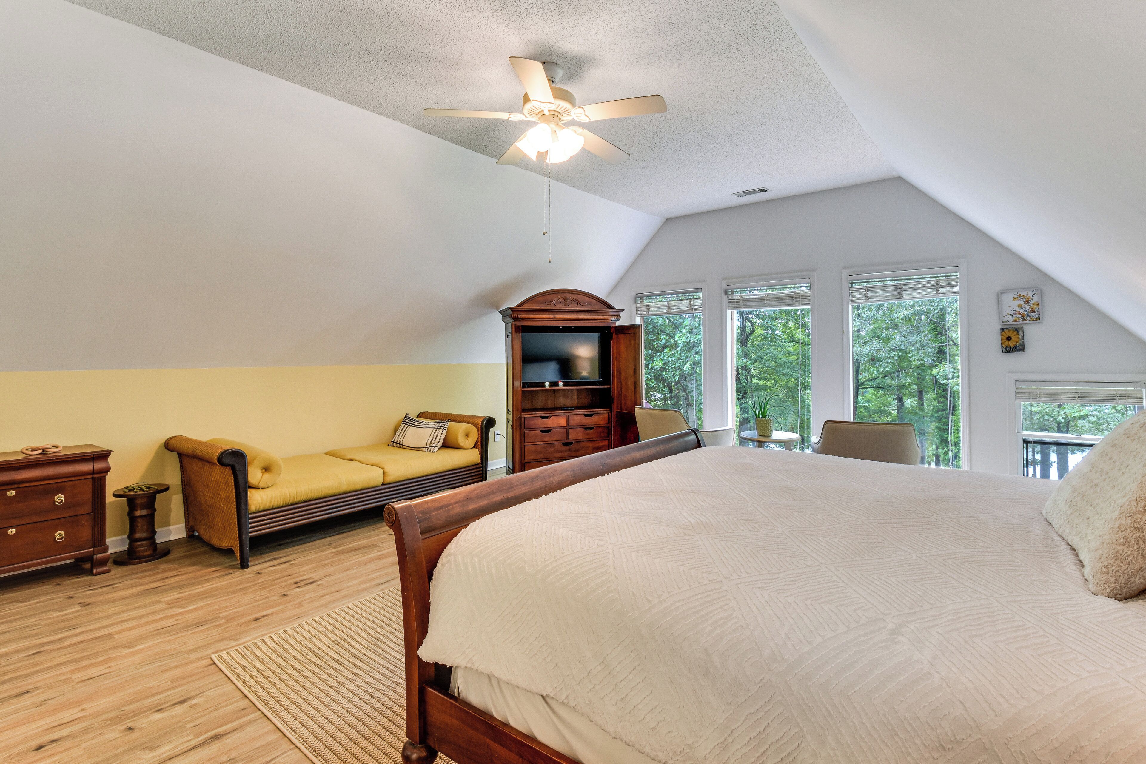 A bedroom with a large bed, a wooden dresser, a yellow armchair, and a ceiling fan.