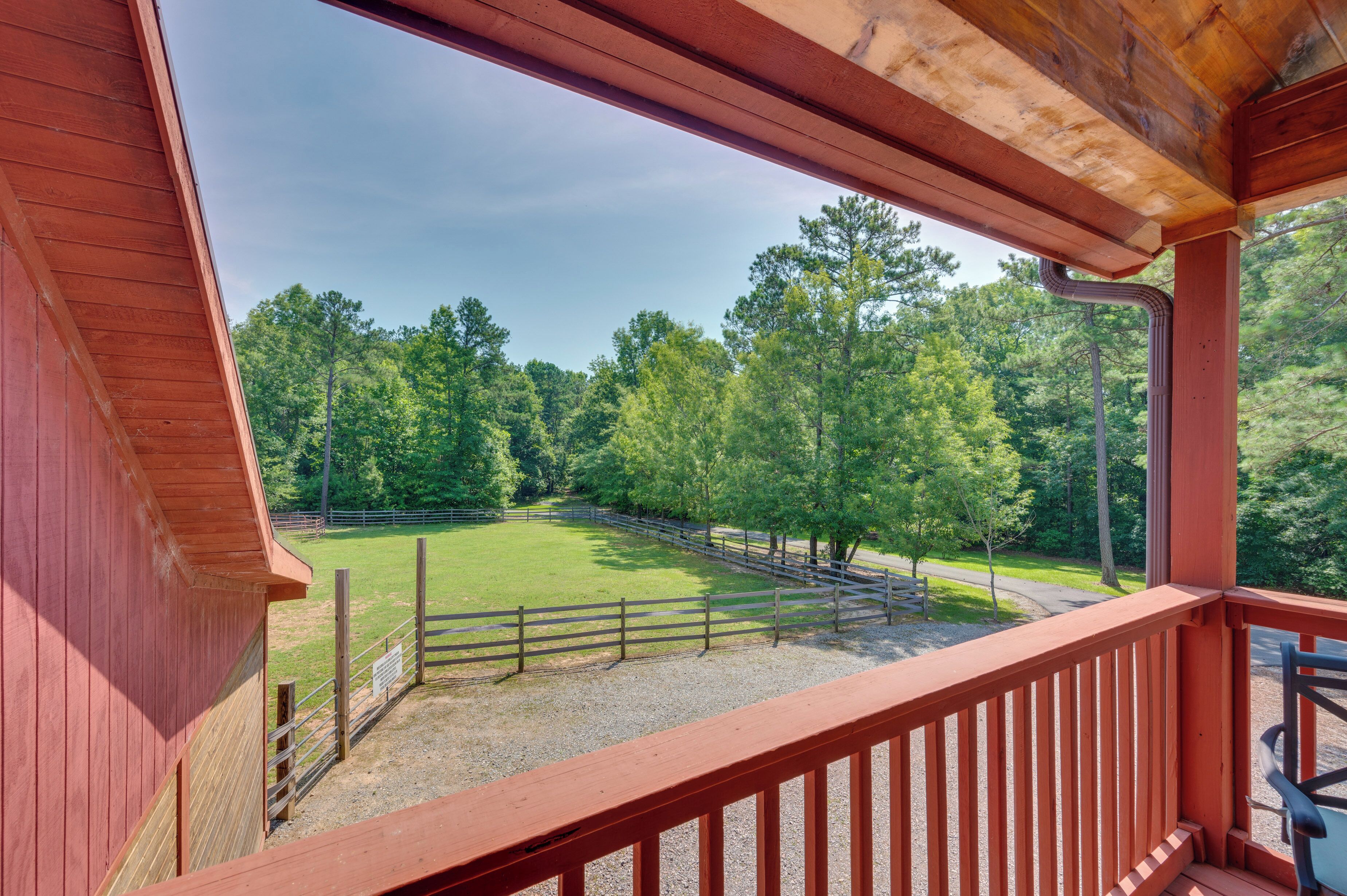 A wooden balcony with a view of a fenced pasture and trees.