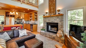 A spacious living area with a stone fireplace, leather sofa, and a high ceiling with wooden beams.