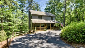 A two-story house with a porch, surrounded by dense forest.