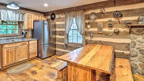 A rustic kitchen with wooden cabinets, a large wooden table, and a stone wall. - Cozy Creekside Mountain Escape w/ Hot Tub! (Sautee Nacoochee)
