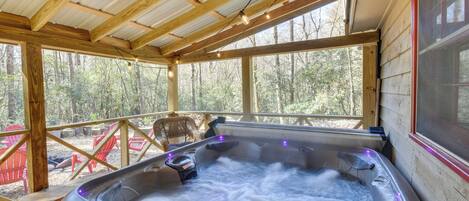 Een hottub in een overdekte buitenruimte met houten balken, omringd door stoelen en uitzicht op bomen.