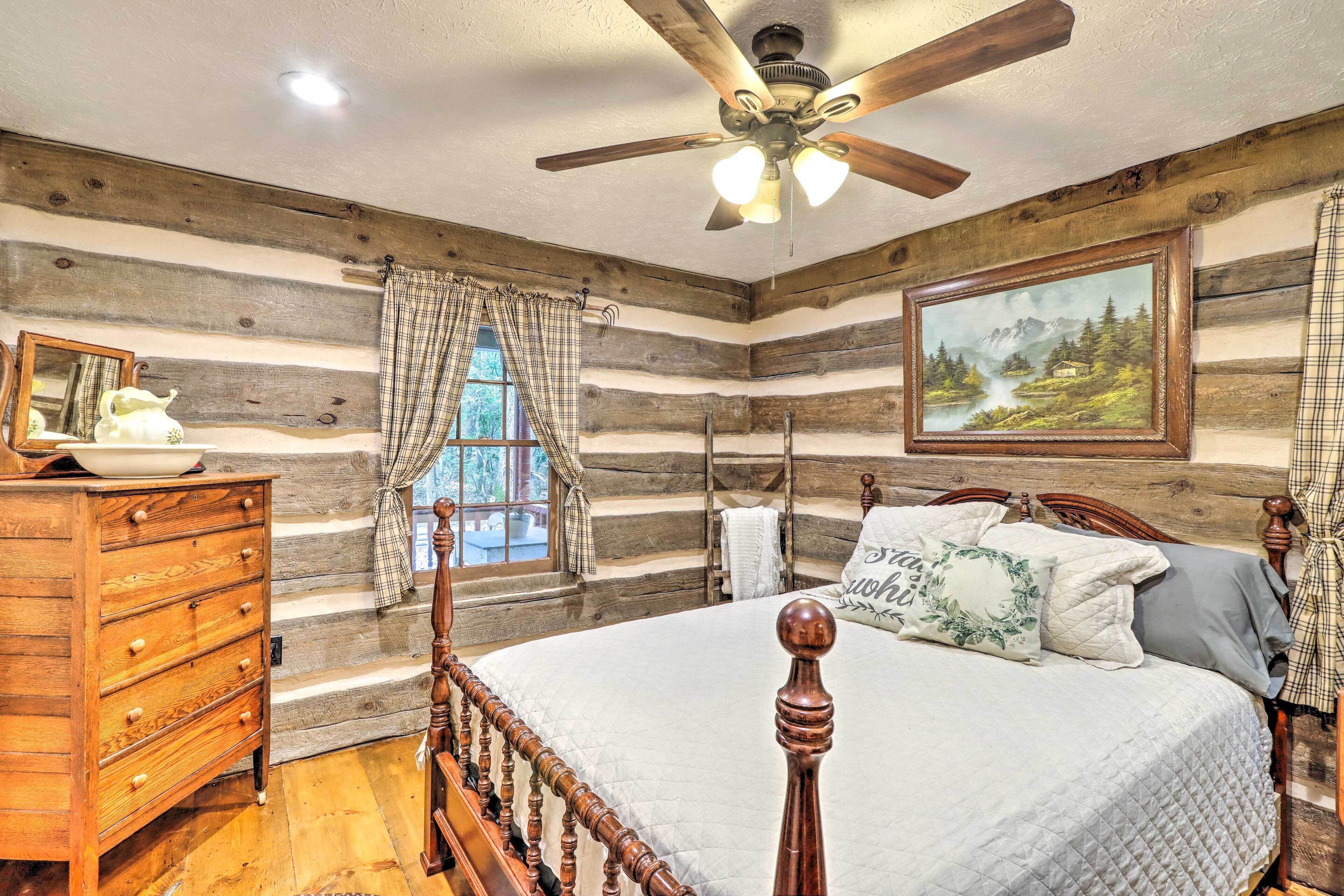 A log cabin-style bedroom with a wooden bed, a dresser, a ceiling fan, and a painting on the wall.