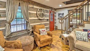 A log cabin interior with a wooden staircase, plaid curtains, a large wheel, and a red door. - Cozy Creekside Mountain Escape w/ Hot Tub! (Sautee Nacoochee)