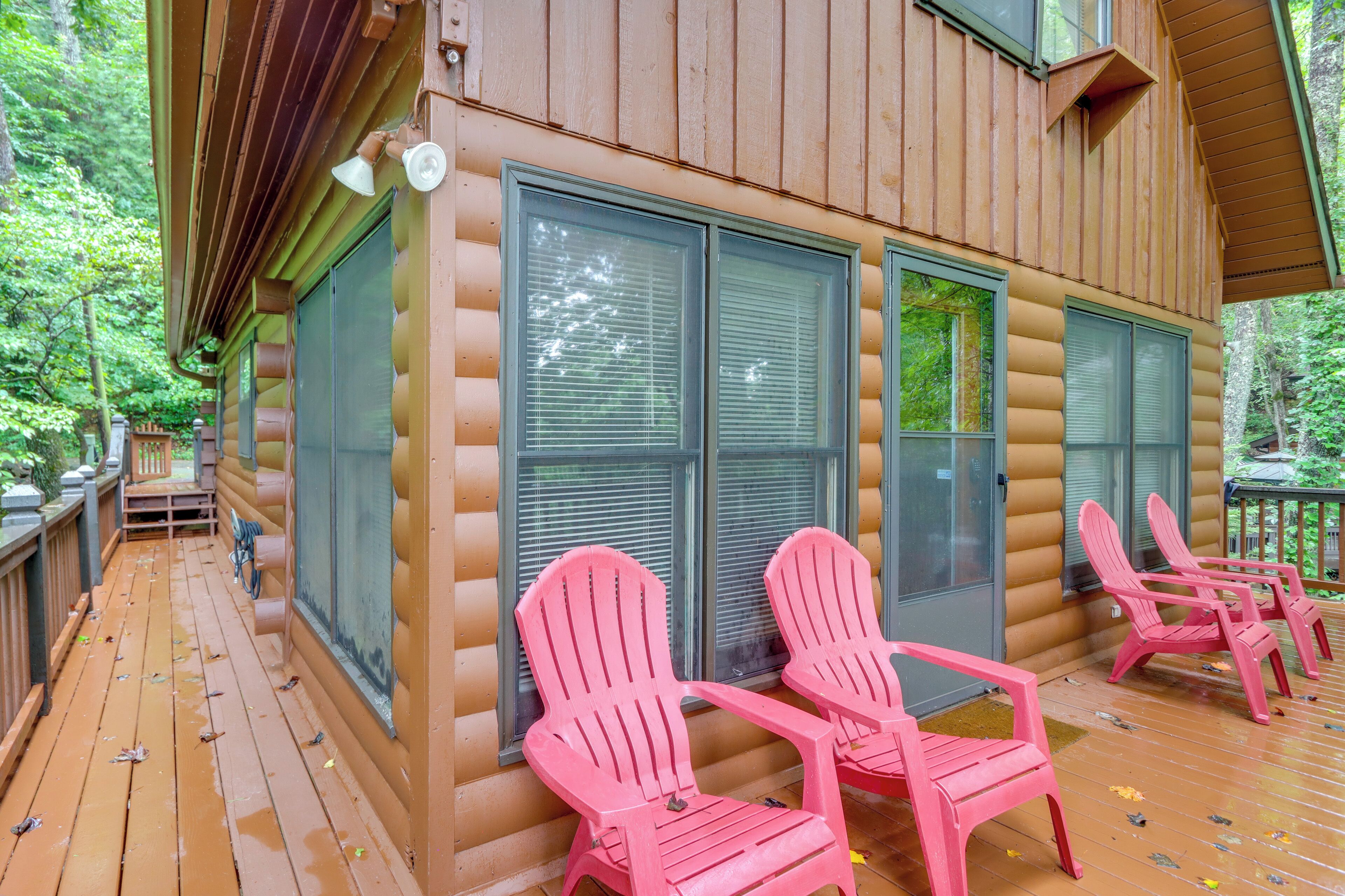 A log cabin with a wooden deck, two pink Adirondack chairs, and large windows.