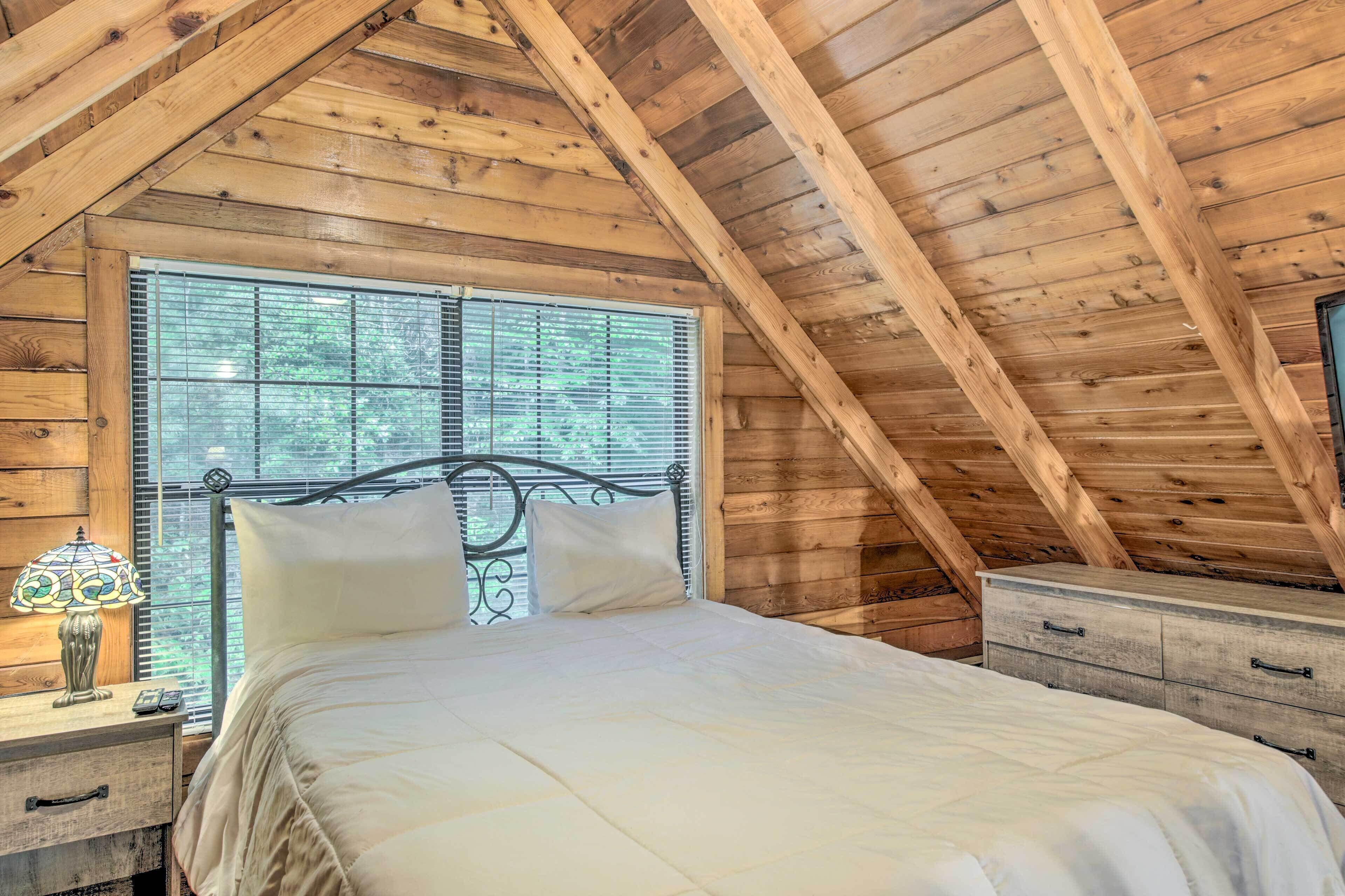 Un dormitorio de madera con cama, mesita de noche, cómoda y ventana con persianas.