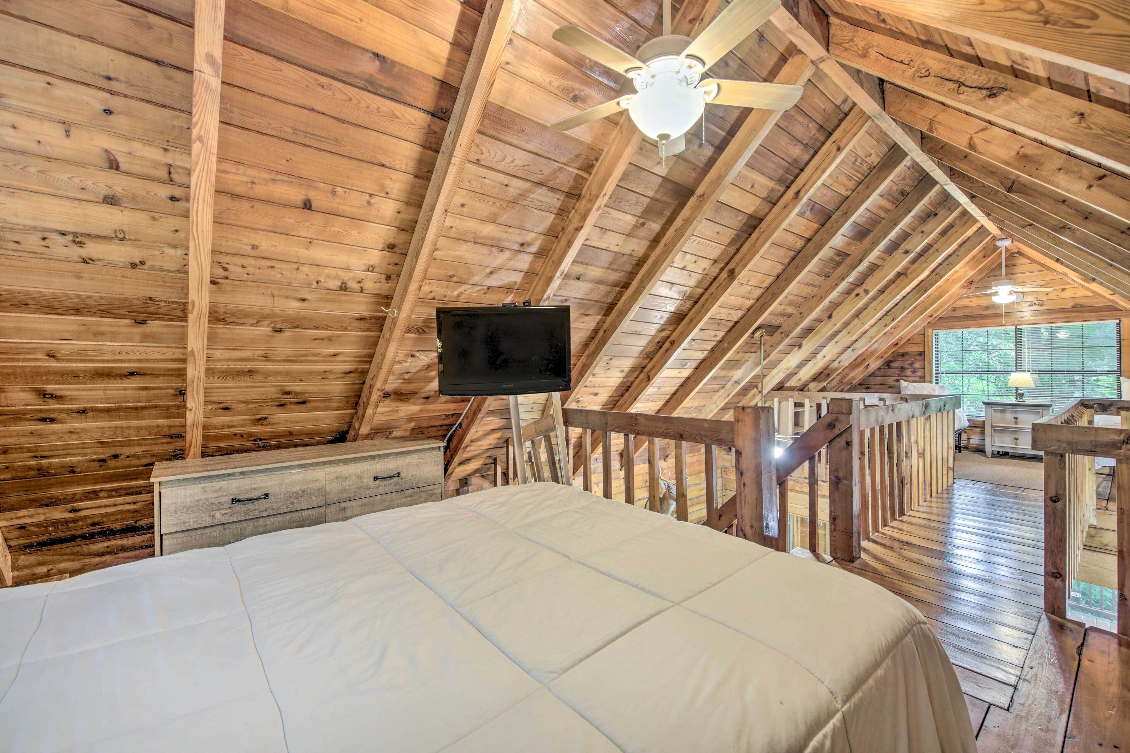 A bedroom with a wooden ceiling, a bed, a TV, and a window.