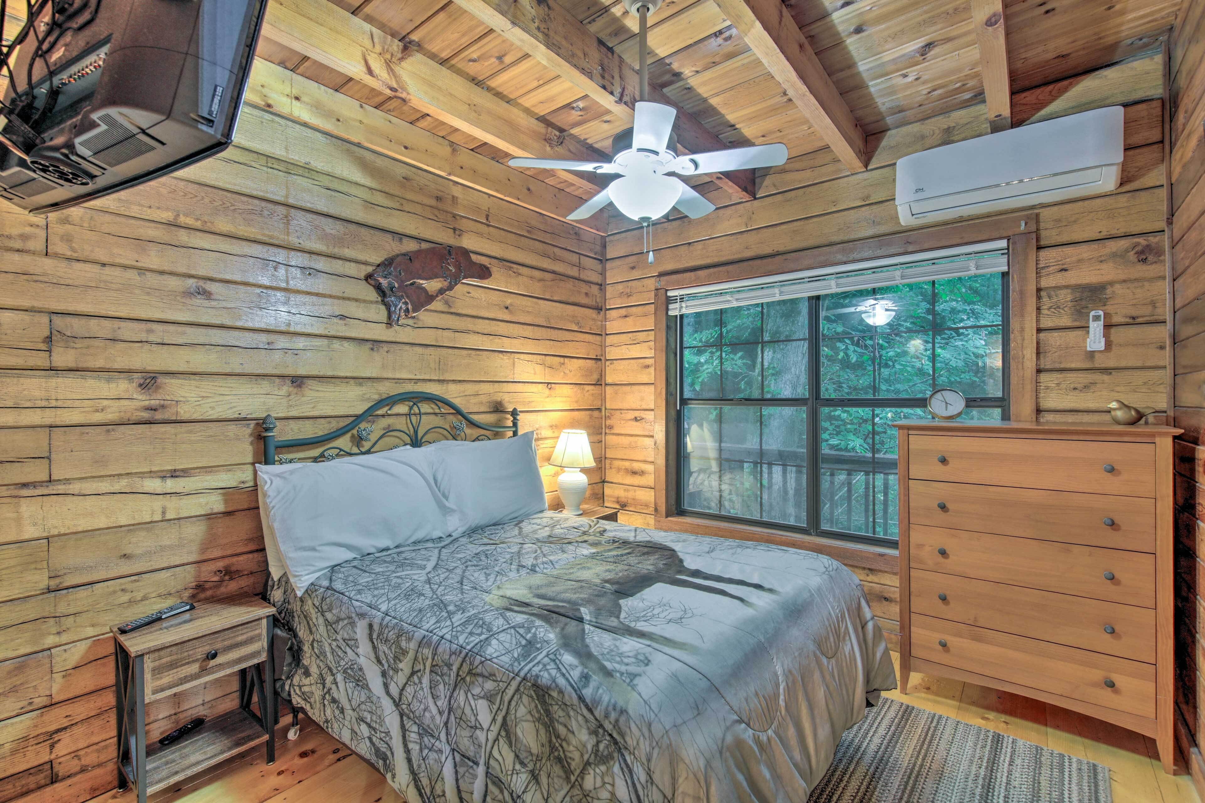 A wooden cabin room with a bed, dresser, window, and ceiling fan.