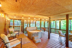 Una terraza de madera con jacuzzi, asientos e iluminación colgante.