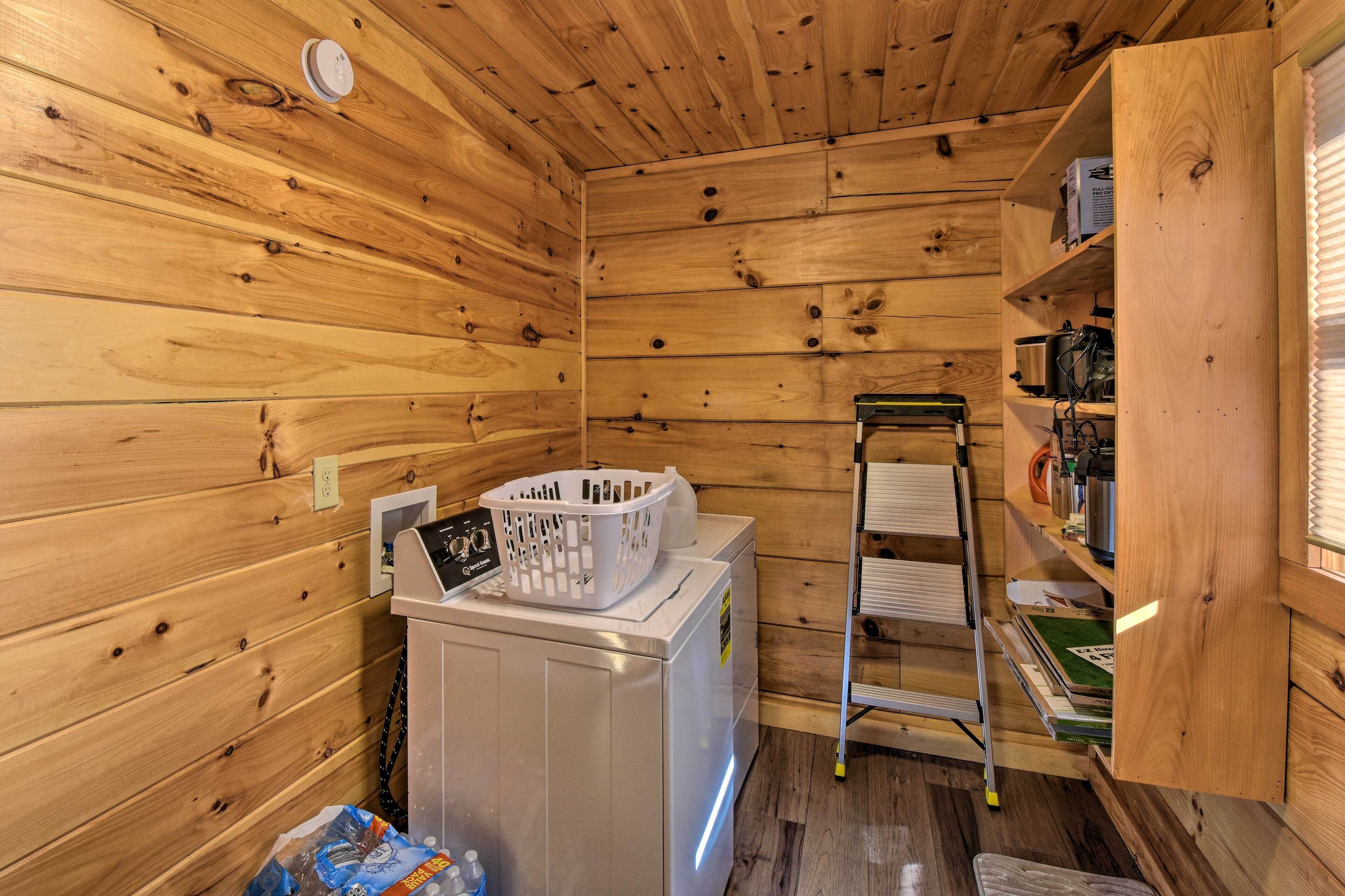 Une petite pièce aux murs en bois, équipée d’un lave-linge, d’un étendoir et d’une petite étagère sur laquelle sont disposés divers objets.