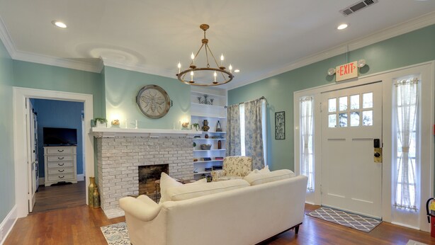 A living room with a white sofa, a fireplace, a chandelier, and a door with an exit sign. - 'the Inn on Second' - Jackson Family Home! (Jackson)
