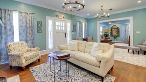A living room with a sofa, armchair, and a chandelier. There is a door with an exit sign, and a window with curtains. - 'the Inn on Second' - Jackson Family Home! (Jackson)