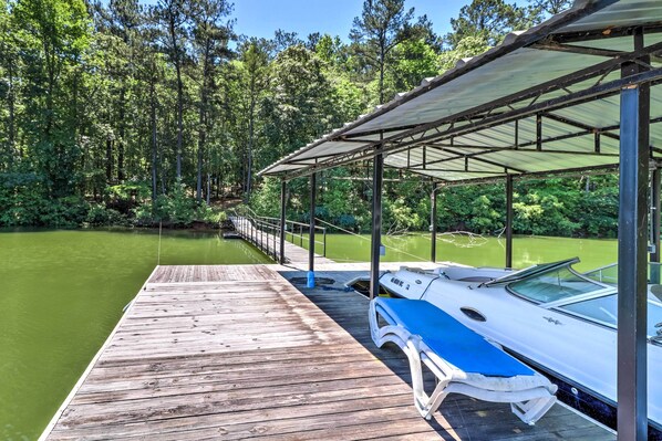 A wooden dock extending into a calm body of water, with a covered boat area and a forested backdrop. - Waterfront West Point Lake Cabin w/ Private Dock! (LaGrange)