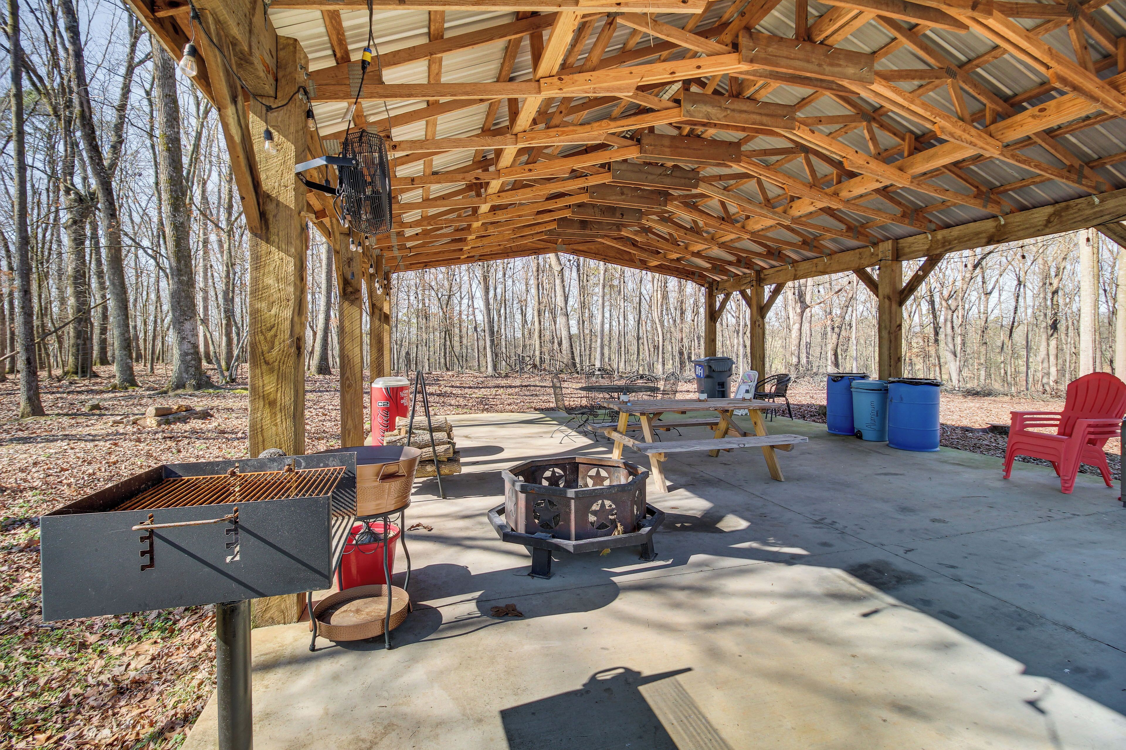 An outdoor covered area with a grill, a fire pit, picnic tables, and chairs.