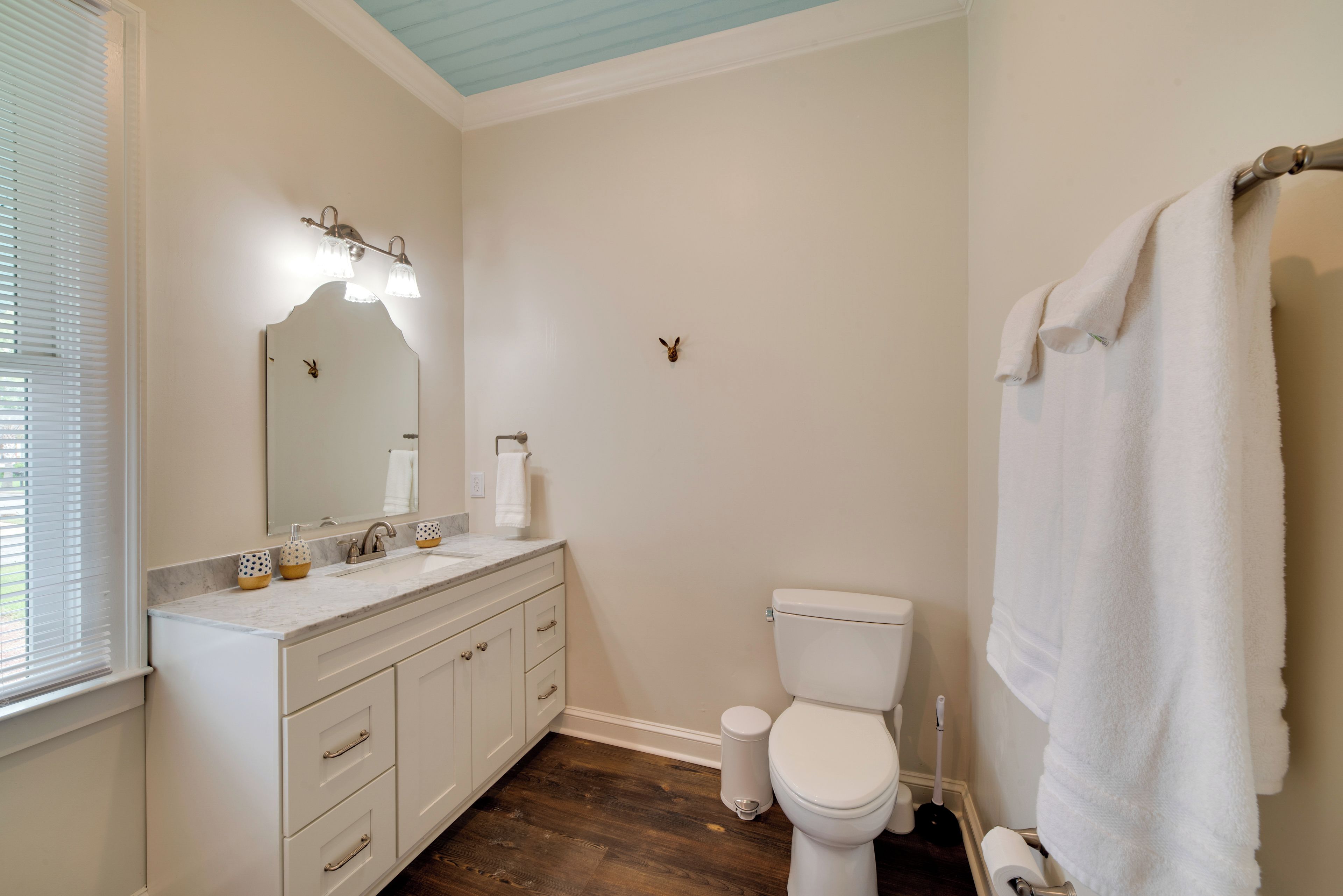 A bathroom with a white sink, mirror, and toilet. There is a towel hanging on the wall.
