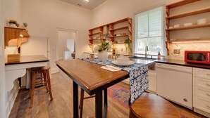 A kitchen with a wooden table, white cabinets, a red microwave, and a window with blinds. - Restored Home Near Downtown Thomasville (Thomasville)