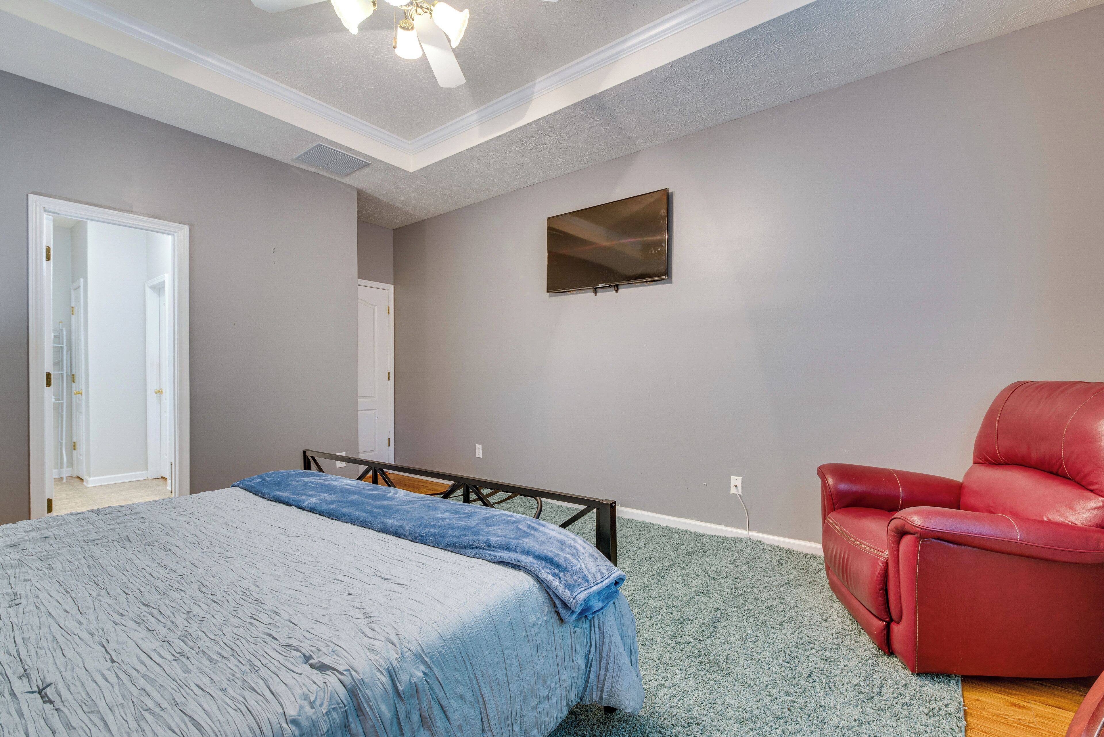 A bedroom with a bed, a red chair, a TV, and a door.