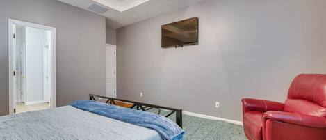 A bedroom with a bed, a red chair, a TV, and a door.