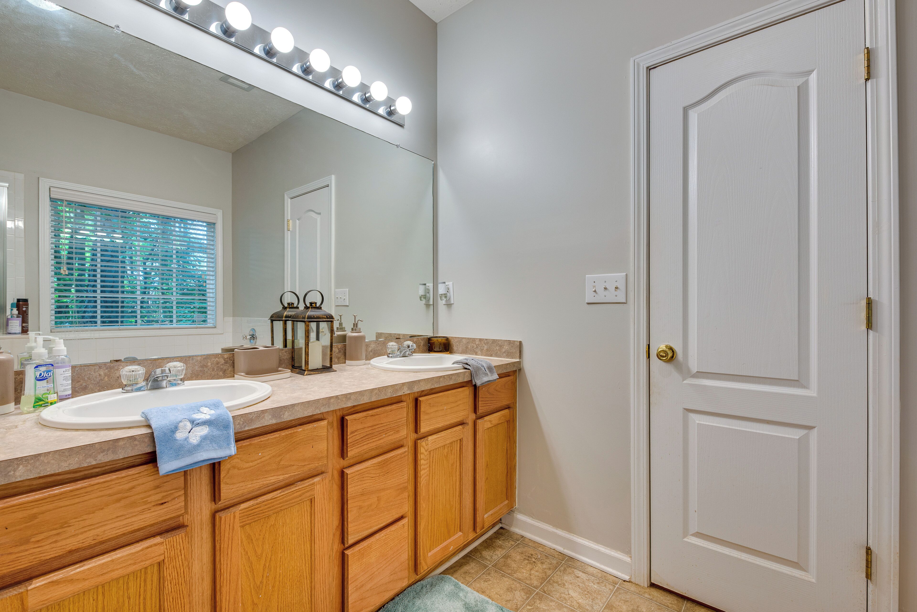 A bathroom with two sinks, wooden cabinets, a vanity mirror, and a door with a light switch.